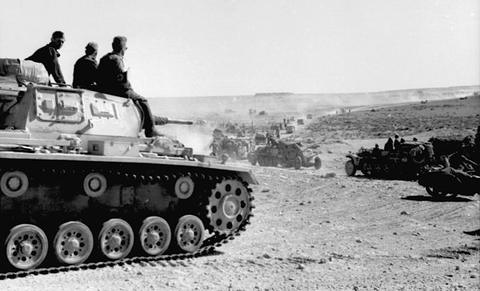 Period photograph: three men sitting on a tank turret, vehicles in a dust cloud behind
