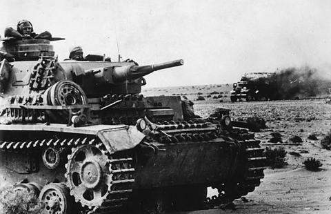 Period photograph: a tank in the foreground, a vehicle on fire in the background