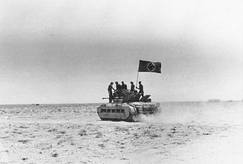 Period photograph: a tank with men on top and a flag on a pole in open desert
