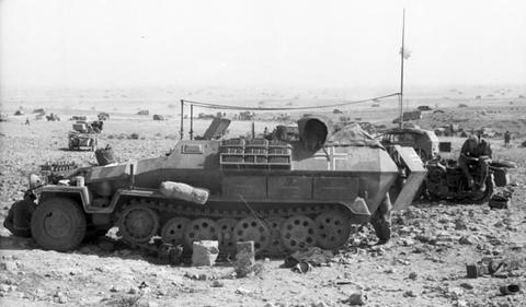 Period photograph: a half-track and a motorcycle among scattered equipment in the desert