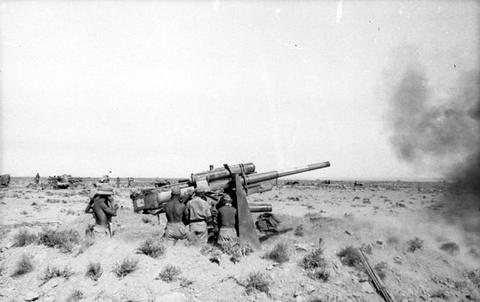 Period photograph: a gun firing across flat ground, smoke on the right