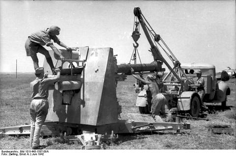 Period photograph: soldiers working on a gun while a crane lifts its barrel