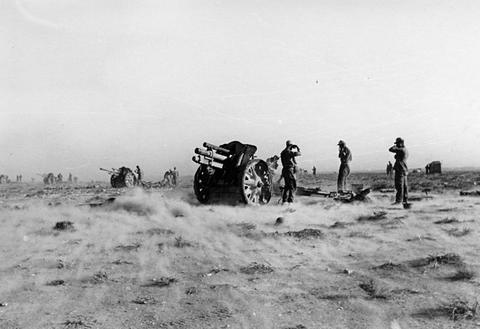 Period photograph: gunners at a field howitzer on scrubby desert ground