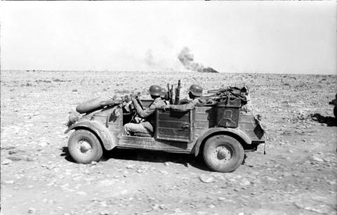 Period photograph: a small open car with soldiers crossing stony ground
