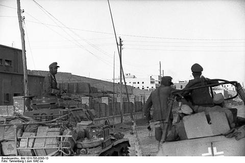 Period photograph: men in a half-track and on a tank in a street with telegraph poles