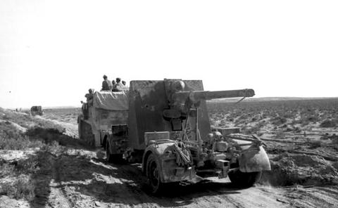 Period photograph: a half-track towing a large gun across rough ground
