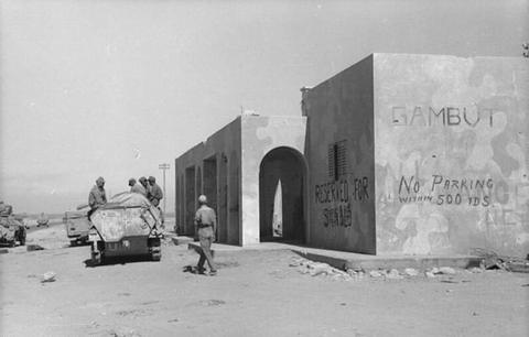 Period photograph: soldiers and a vehicle beside a white building with painted lettering