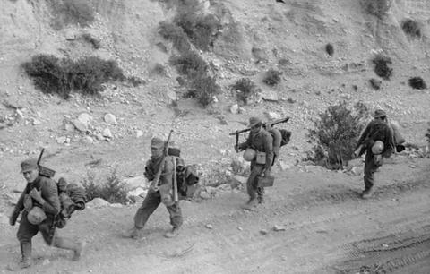Period photograph: four soldiers walking along a rocky hillside track