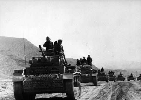 Period photograph: a line of tanks with men on top driving along a dusty track