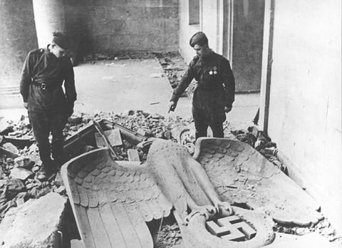 Period photograph: two Soviet soldiers in a ruined hall beside a large fallen eagle emblem