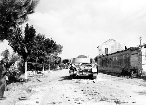 Period photograph: a knocked-out tank on a dusty road beside a station building