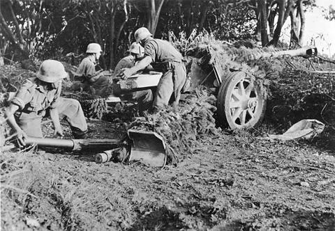 Period photograph: soldiers loading an anti-tank gun in a camouflaged position