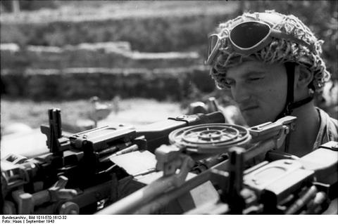 Period photograph: a paratrooper with sunglasses on his helmet behind a twin machine gun