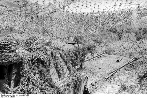 Period photograph: a tank turret set low in the ground under a large camouflage net