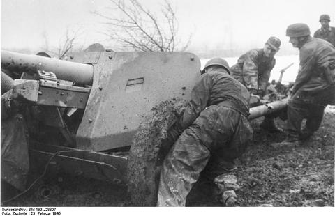 Period photograph: paratroopers pushing an anti-tank gun across rough ground