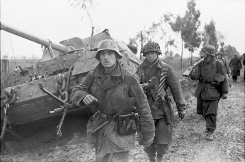 Period photograph: a column of infantry on a muddy road passing a large tank destroyer