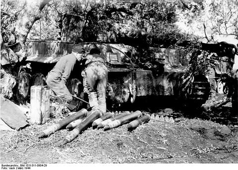 Period photograph: crewmen working on a Tiger tank parked under trees, shells lined up in front