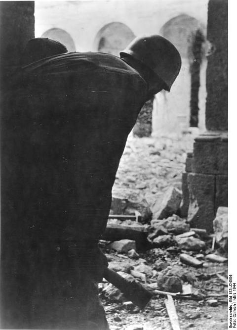Period photograph: a paratrooper holding a stick grenade among the rubble of a vaulted ruin