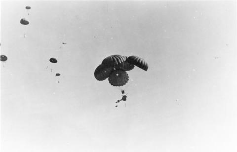 Period photograph: a gun load hanging beneath a cluster of parachutes against the sky