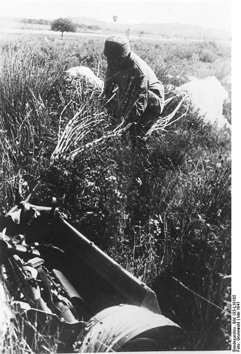 Period photograph: a paratrooper in tall grass beside a long metal container