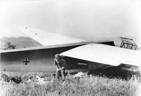 Period photograph: a landed glider in a field, a paratrooper beside the fuselage