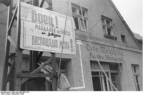 Period photograph: a large painted sign in Cyrillic letters fixed to the front of a town building