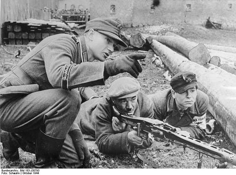 Period photograph: men in caps and coats lying behind a machine gun, an instructor kneeling beside them