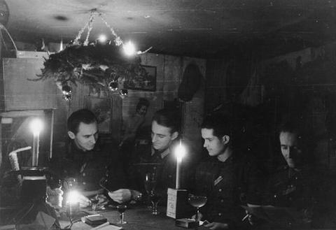 Period photograph: soldiers seated at a table lit by candles in a timber-lined dugout