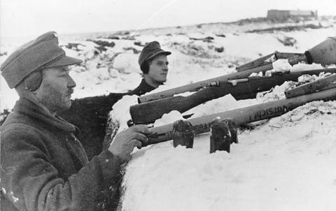 Period photograph: men in field caps and coats holding Panzerfausts and rifles against a snowy background