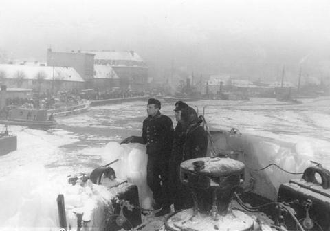 Period photograph: sailors on the snowy bow of a ship in a frozen harbour, people on the quay beyond