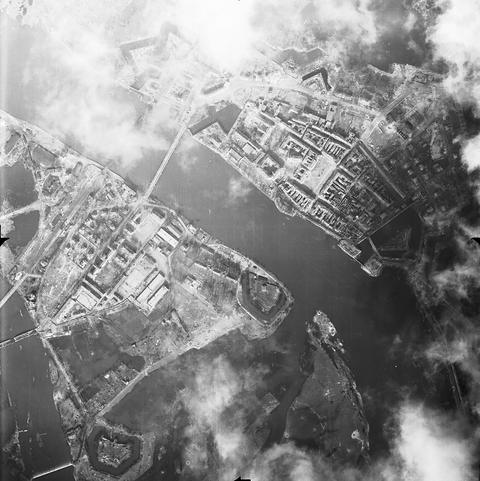 Period photograph: aerial view of a bastioned fortress town on a river, with bridges, damaged buildings and patches of cloud