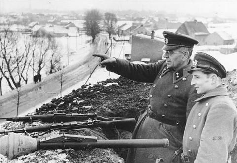 Period photograph: men in caps behind an earth parapet, Panzerfausts laid ready on top, one man pointing