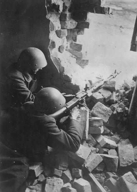 Period photograph: two men in steel helmets crouching with a machine gun beside a broken brick wall