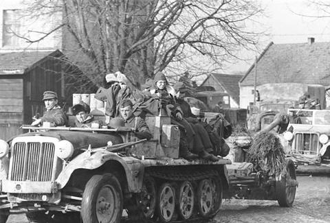 Period photograph: soldiers seated on a small half-track towing a field gun along a village road