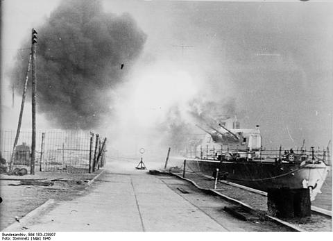 Period photograph: a warship at a quay with a large cloud of gun smoke rising over it