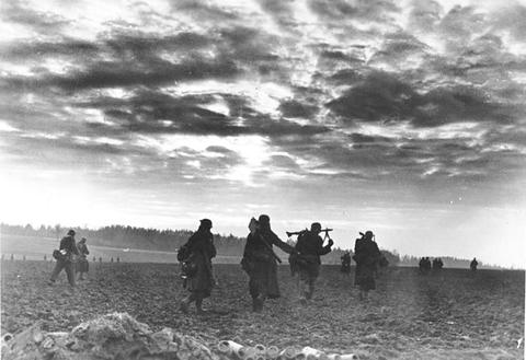 Period photograph: small figures of soldiers walking across a flat field under a large cloudy sky