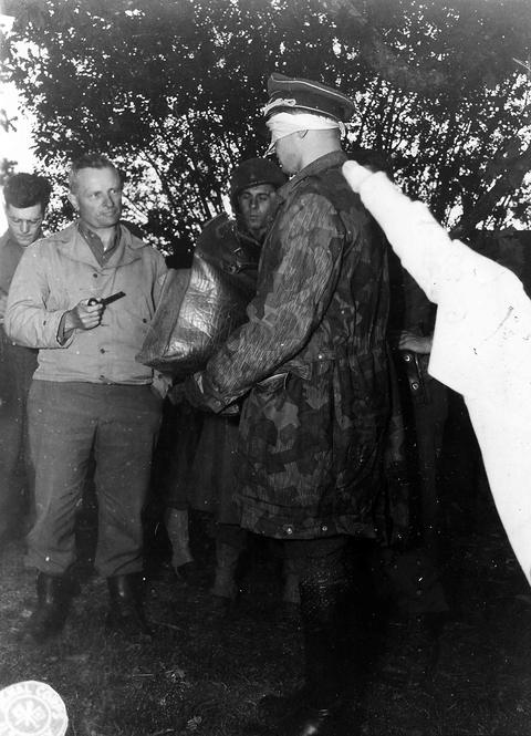 Period photograph: an officer in a camouflage smock with a white cloth, facing American officers in a wood