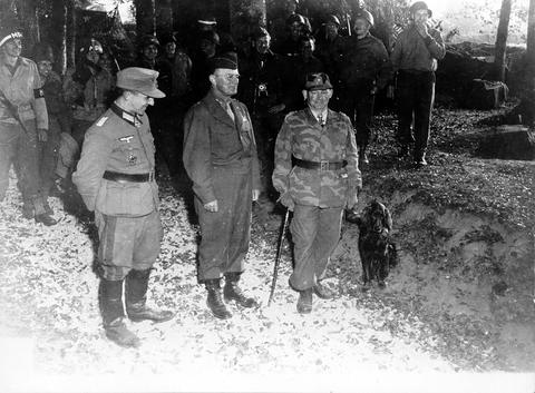 Period photograph: three officers standing on a path, one in a camouflage jacket with a dog at his side, soldiers behind
