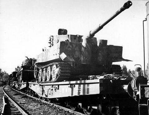 Period photograph: Tiger tanks in camouflage paint loaded on railway flatcars beside a track