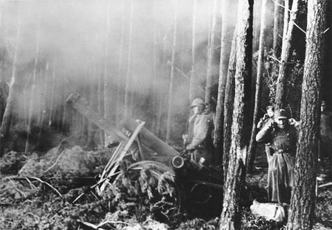 Period photograph: a heavy gun firing in a pine wood, smoke rising, its crew among the trunks