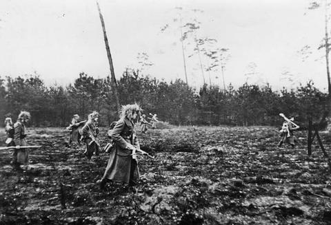 Period photograph: soldiers with rifles spread out across a muddy clearing in front of a treeline