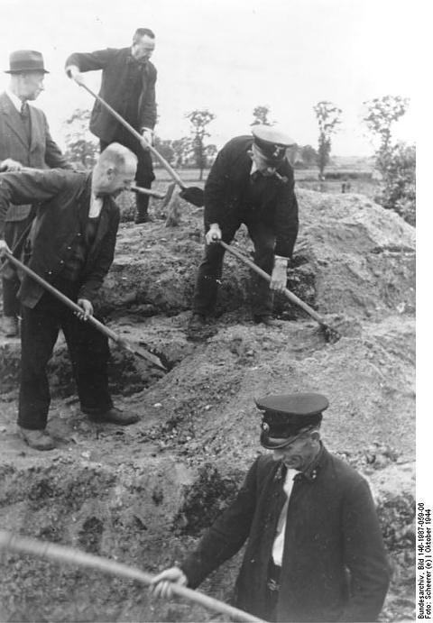 Period photograph: men in hats and caps digging with shovels on a heap of earth